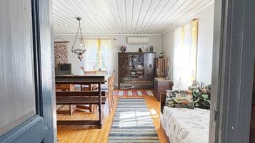 A room with a wooden floor, a dining table with chairs, a sofa, a cabinet, and a hanging light fixture.
