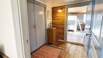 A wooden-floored hallway with a striped rug, a wooden wall, and a door leading to a room.
