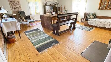 A room with a wooden floor, a dining table with chairs, a bench, a sofa, and a small table with a lamp.