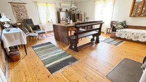 A spacious living room with a wooden floor, a dining area with a table and chairs, a sofa, and a bench. - 4 Person Holiday Home in Furuby (Hovmantorp)