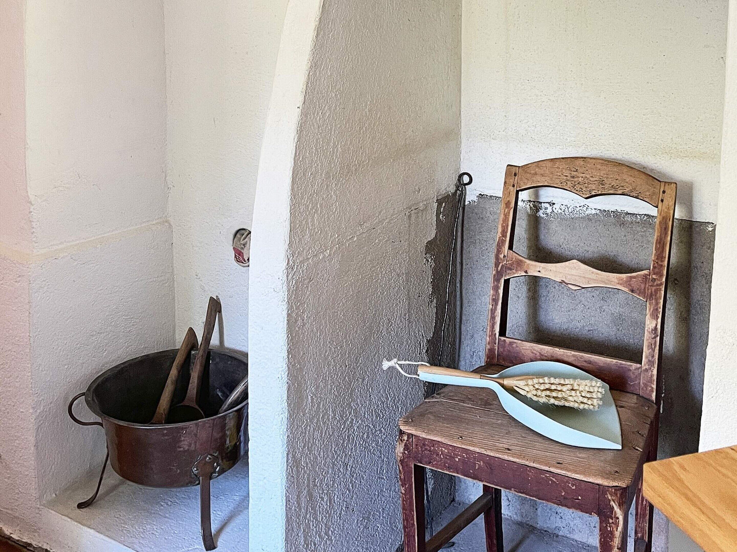 Een eenvoudige kamer met een houten stoel, een metalen pot en een houten lepel.