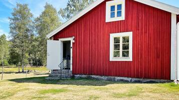 A red barn with a white door and window, surrounded by grass and trees.