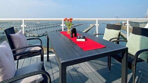 A deck with wicker chairs and a table, overlooking a marina with boats and docks.