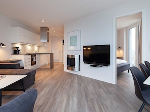 A modern apartment with a kitchen, dining area, living room, and a bedroom with a TV.
