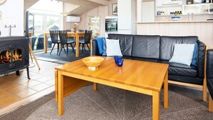 Ett mysigt vardagsrum med en soffa, ett träbord, en öppen spis och en matplats med stolar och ett bord.