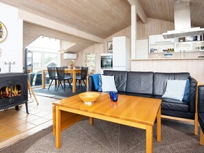 Un salon chaleureux avec un canapé, une table en bois, une cheminée et un coin repas comprenant des chaises et une table.