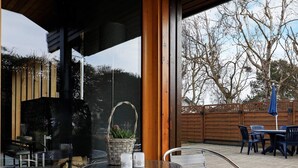 An outdoor patio with a round table and metal chairs, a wicker basket with flowers, and a view of a wooden fence and trees. - 6 Person Holiday Home in Laeso (Læsø)