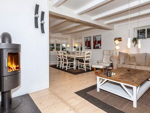 Ein modernes Wohnzimmer mit Kaminofen, einem Essbereich mit weißen Möbeln und einem Sofa mit gemustertem Teppich.