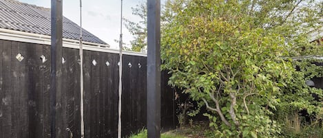 A wooden swing set in a backyard with a wooden fence and a tree.