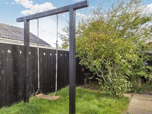 A wooden swing set in a backyard with a wooden fence and a tree.