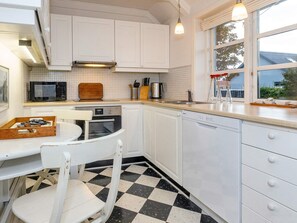 A kitchen with white cabinets, a microwave, an oven, a dishwasher, and a checkered floor. - 4 Star Holiday Home in Skagen (Skagen)