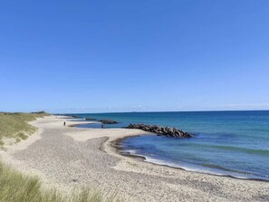 A beach with a rocky breakwater, clear skies, and a person walking. - 4 Star Holiday Home in Skagen (Skagen)