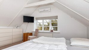 A bedroom with a sloped ceiling, a bed with white bedding, a chair, a dresser, a television, and a window with a view. - 4 Star Holiday Home in Skagen (Skagen)
