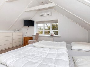 A bedroom with a sloped ceiling, a bed with white bedding, a chair, a dresser, a television, and a window with a view. - 4 Star Holiday Home in Skagen (Skagen)