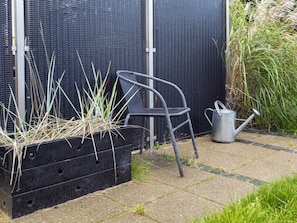 A garden area with a black planter box containing plants, a metal chair, and a watering can. - 4 Star Holiday Home in Skagen (Skagen)