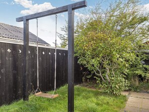 A wooden swing set in a backyard with a wooden fence and a tree. - 4 Star Holiday Home in Skagen (Skagen)