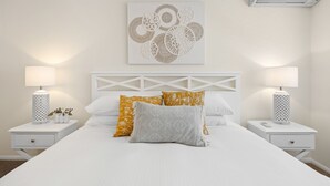 A neatly arranged bedroom with a white bed, two bedside tables with lamps, and a wall-mounted air conditioner. - Regency 3 Bedroom Central Town House (Sunshine Coast)