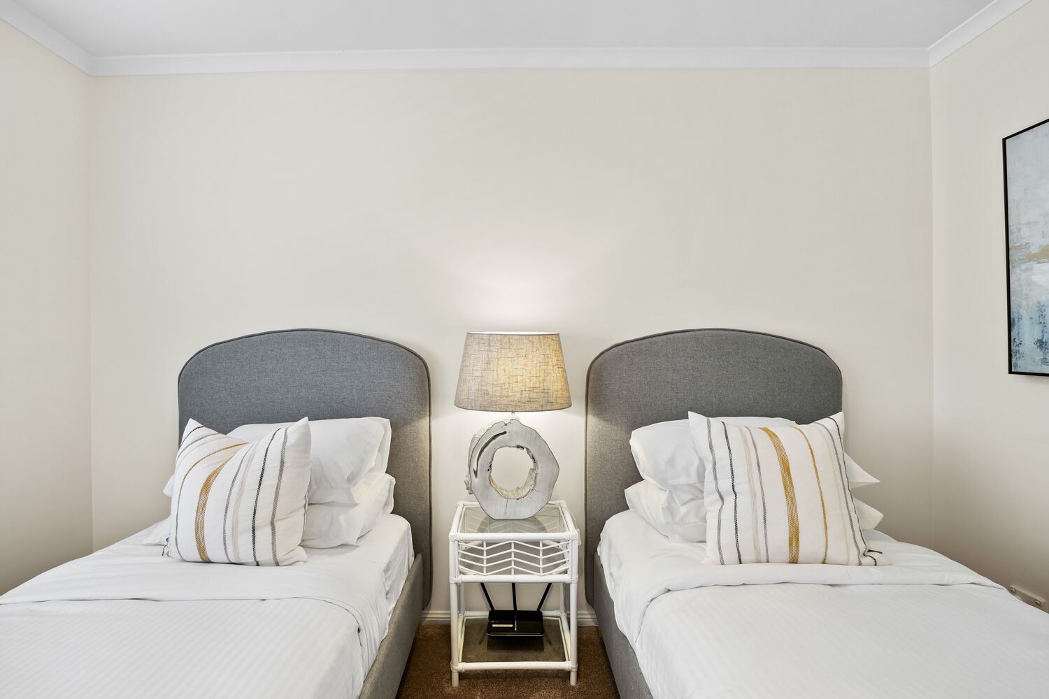 A hotel room with two single beds, a nightstand with a lamp, and a framed picture on the wall.