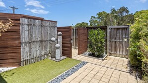 A fenced backyard with a wooden gate, a small tree, and a paved pathway. - Regency 3 Bedroom Central Town House (Sunshine Coast)