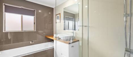 A modern bathroom with a glass-enclosed shower, a white bathtub, and a vanity with a wooden countertop.