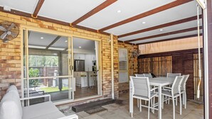 A covered patio with a dining table and chairs, a sliding glass door leading to a kitchen, and a brick wall. - Regency 3 Bedroom Central Town House (Sunshine Coast)