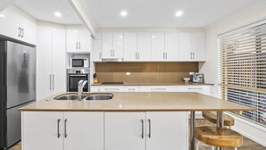 A modern kitchen with white cabinets, stainless steel appliances, and a wooden countertop. - Regency 3 Bedroom Central Town House (Sunshine Coast)