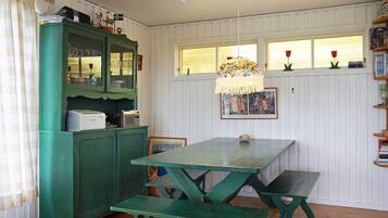 Une pièce avec une table verte et des bancs, un meuble avec des portes en verre et une fenêtre avec des rideaux.