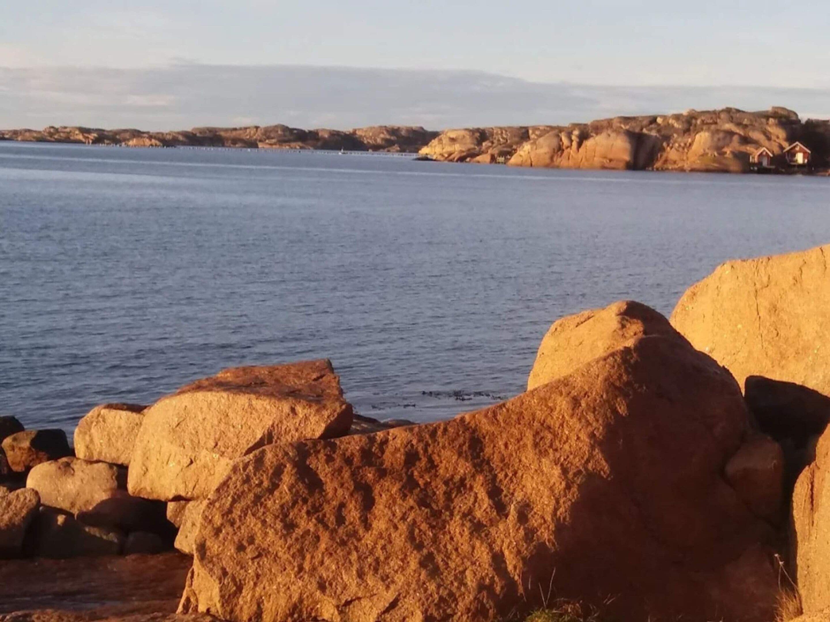 A coastal landscape with large rocks in the foreground and a calm sea in the background.