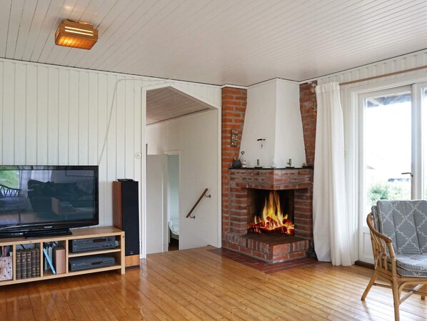Una sala de estar con chimenea de ladrillo, un televisor sobre un soporte de madera y un sillón de mimbre.