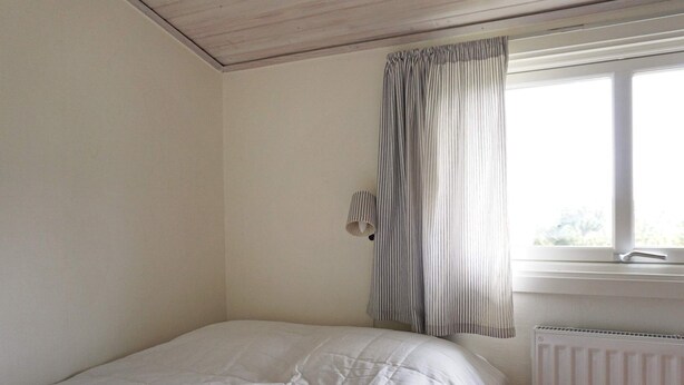 Un dormitorio con una cama individual, una ventana con cortinas, una lámpara de pared y un radiador.