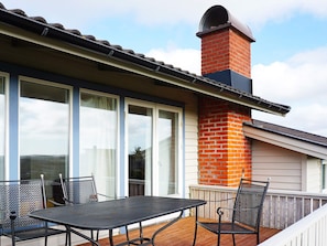 Een terras met een tafel en stoelen, een bakstenen schoorsteen en grote schuifdeuren.