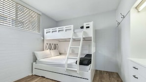 A bunk bed with a ladder, white walls, and a wooden floor.