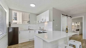 A modern kitchen with white cabinetry, a built-in island with stools, a refrigerator, and a window with blinds.