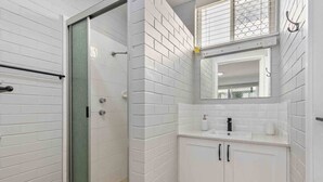 A modern bathroom with white subway tiles, a glass-enclosed shower, a sink with a black faucet, and a mirror above the sink.