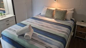 A neatly made bed with striped bedding, a bedside table with a lamp, and a small plant on the nightstand.
