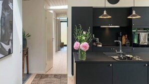 A modern kitchen with black cabinets, a central island, pendant lighting, and a clock on the wall.