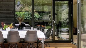 A modern dining area with a glass door leading to an outdoor space, featuring a grill and dining table set.