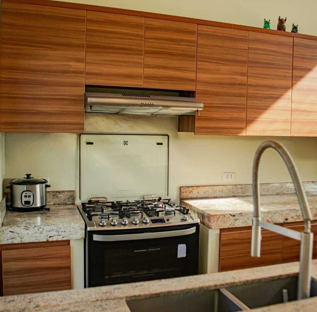 Une cuisine avec des meubles de rangement en bois, un four, un évier et une petite plaque de cuisson électrique.