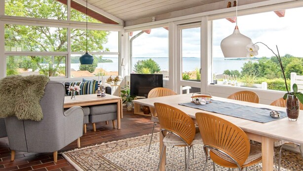A spacious dining area with a view of the sea, a cozy seating area with a fireplace, and large windows offering natural light. - 6 Person Holiday Home in Aabenraa-by Traum (Aabenraa)