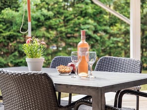 An outdoor dining table with a bottle of Freixenet wine, two glasses, a bowl of nuts, and a potted plant.