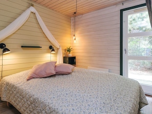 A bedroom with a bed, pillows, bedside lamps, a plant, and a door leading outside.