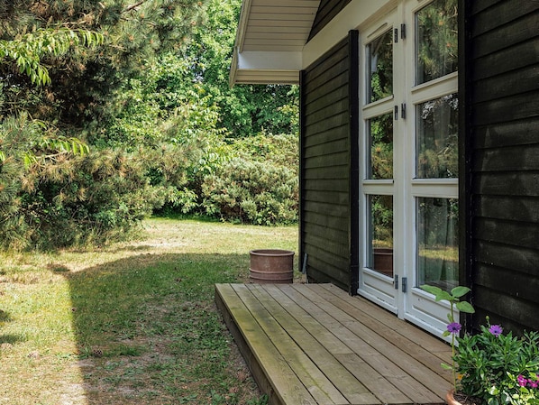 A wooden deck with a window, surrounded by dense greenery.