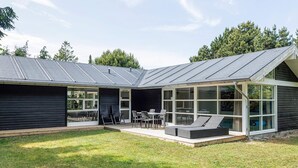 A modern house with a covered patio, outdoor seating, and a large windowed area.