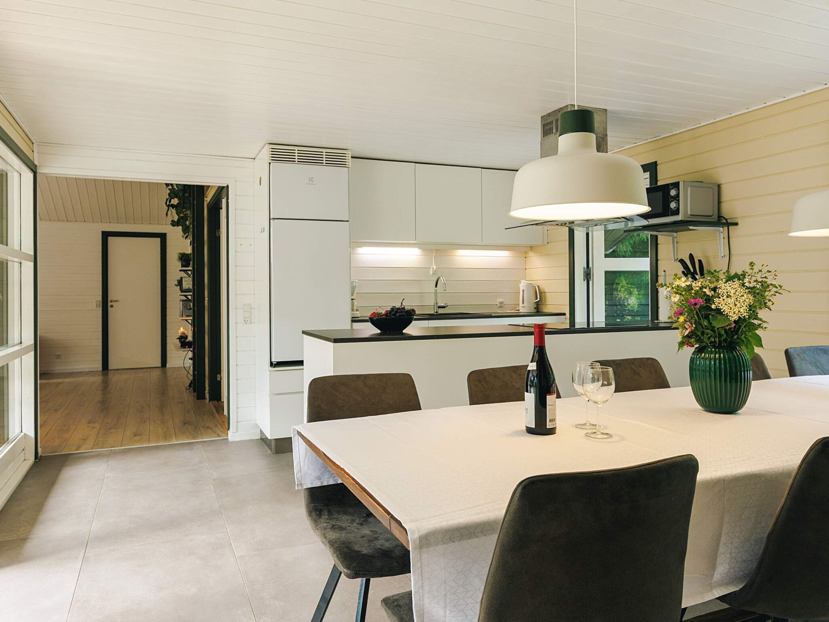 Une cuisine moderne avec des meubles blancs, une table à manger avec des chaises et un vase rempli de fleurs.
