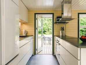 A narrow kitchen with white cabinets, a stainless steel range hood, and a view of the outdoors through an open door.