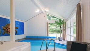 A swimming pool with a blue bench, a hot tub, and a wicker chair.