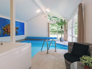 A swimming pool with a blue bench, a hot tub, and a wicker chair.