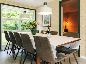 A dining area with a table set for six, chairs, a vase with flowers, a bottle of wine, and a framed picture on the wall.