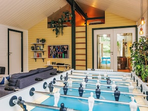 A cozy room with a foosball table, a sofa, a bookshelf, and a ladder leading to a loft area.