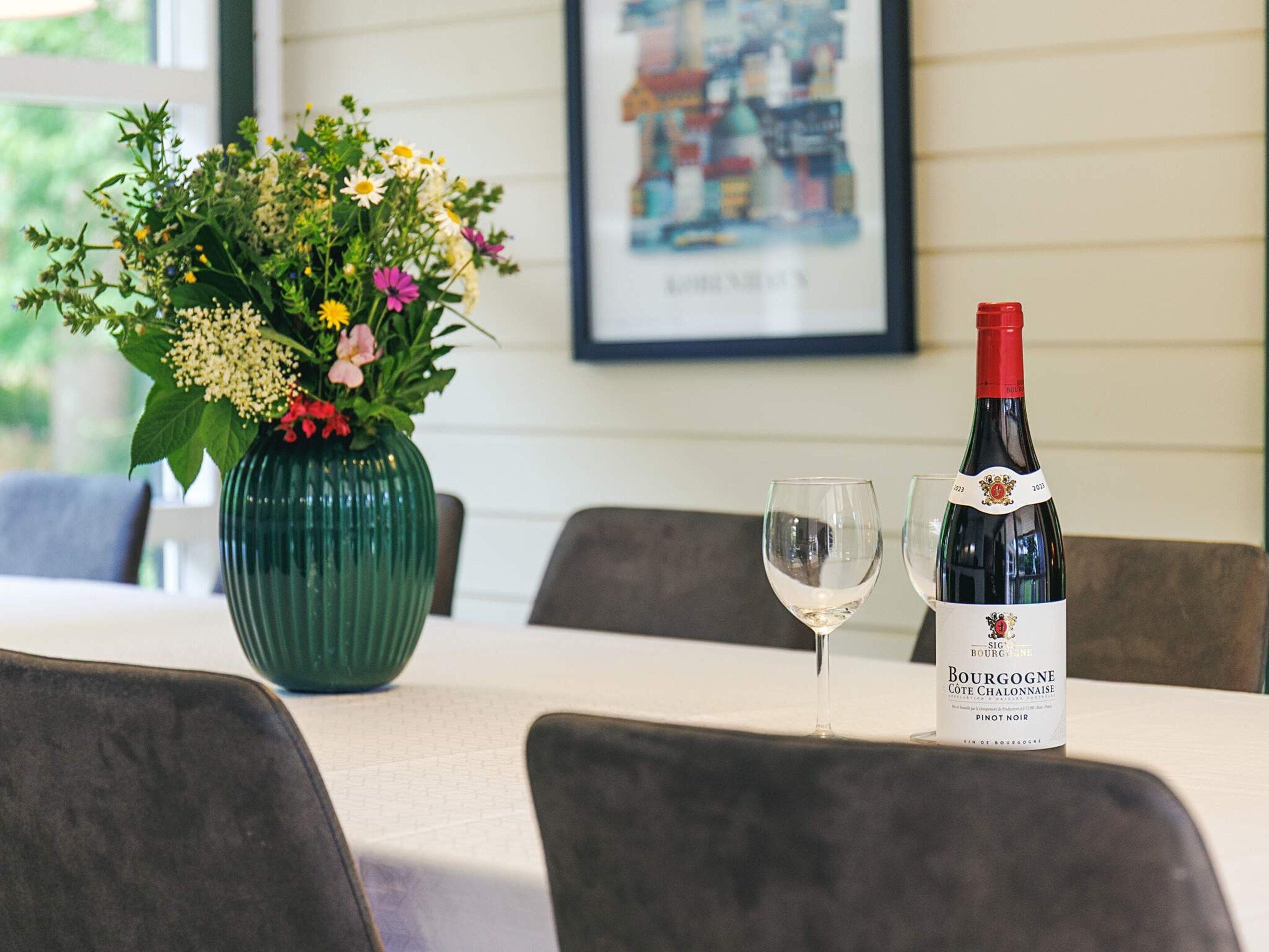 Una mesa con una botella de vino Bourgogne Pinot Noir, una copa y un florero con flores.